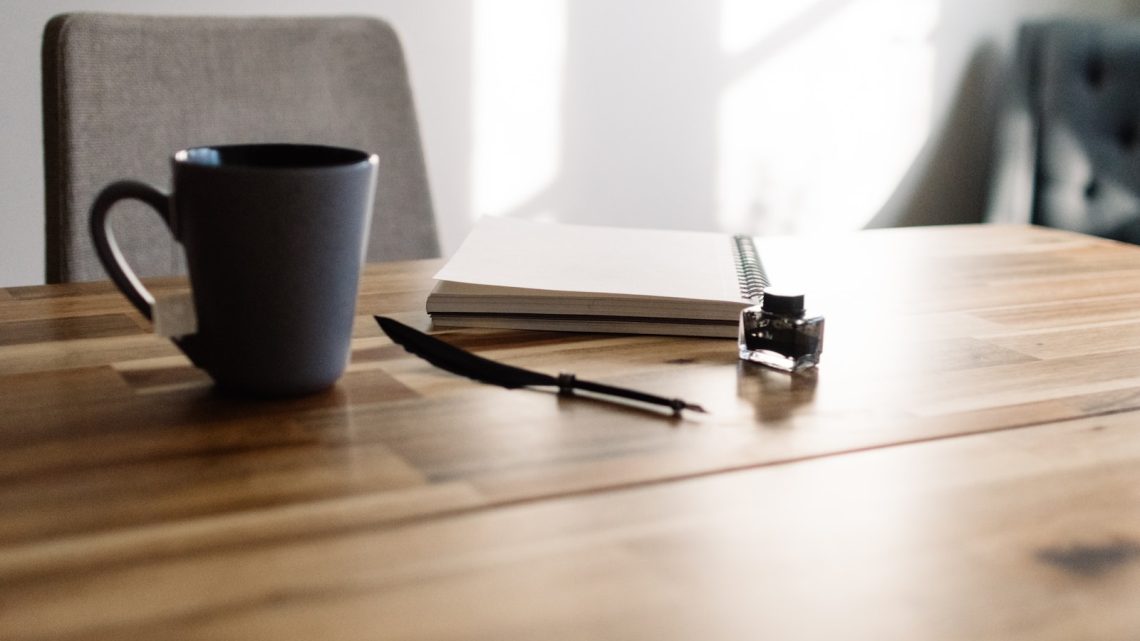 a table with a notebook, pen and a cup of coffee